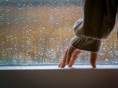 Fotografia d'una mà i una finestra en un dia de pluja.